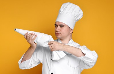 Photo of Portrait of confectioner in uniform holding piping bag on orange background