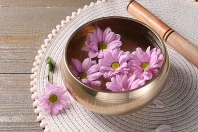 Photo of Tibetan singing bowl with water, beautiful flowers and mallet on wooden table, closeup