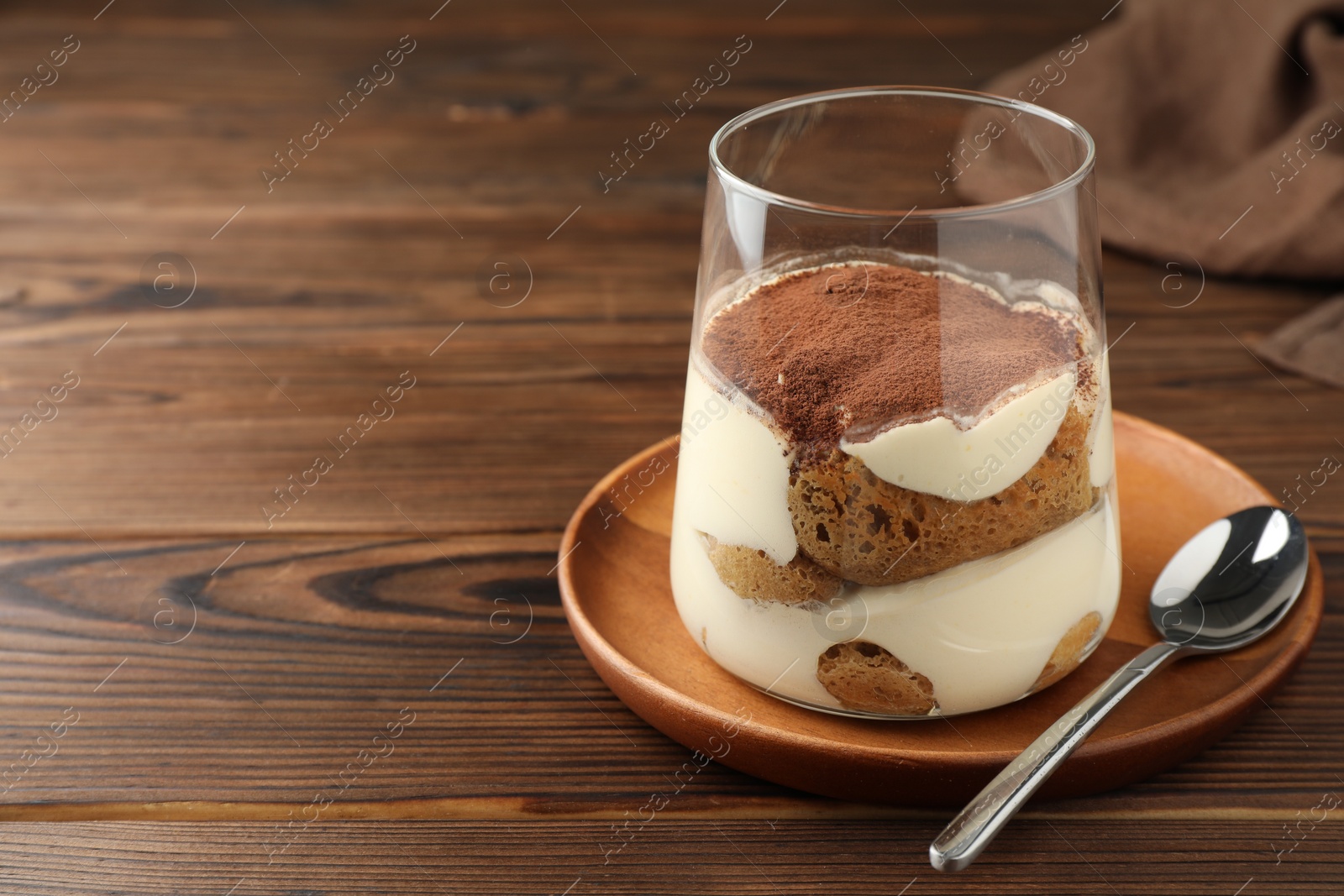 Photo of Delicious tiramisu in glass and spoon on wooden table. Space for text