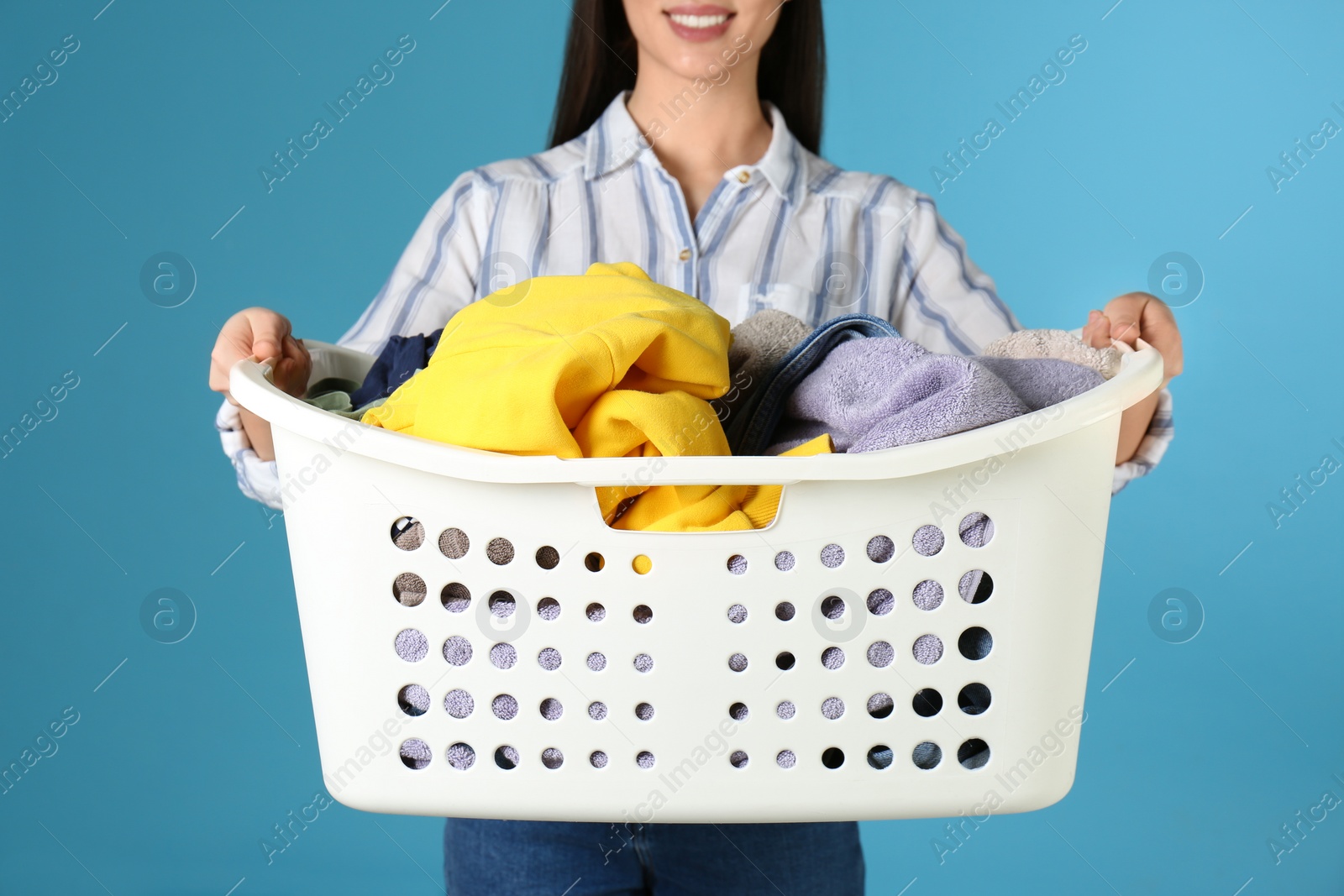 Photo of Young woman holding laundry basket with clothes on color background, closeup