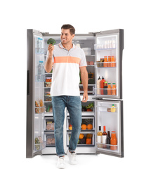 Man with broccoli near open refrigerator on white background