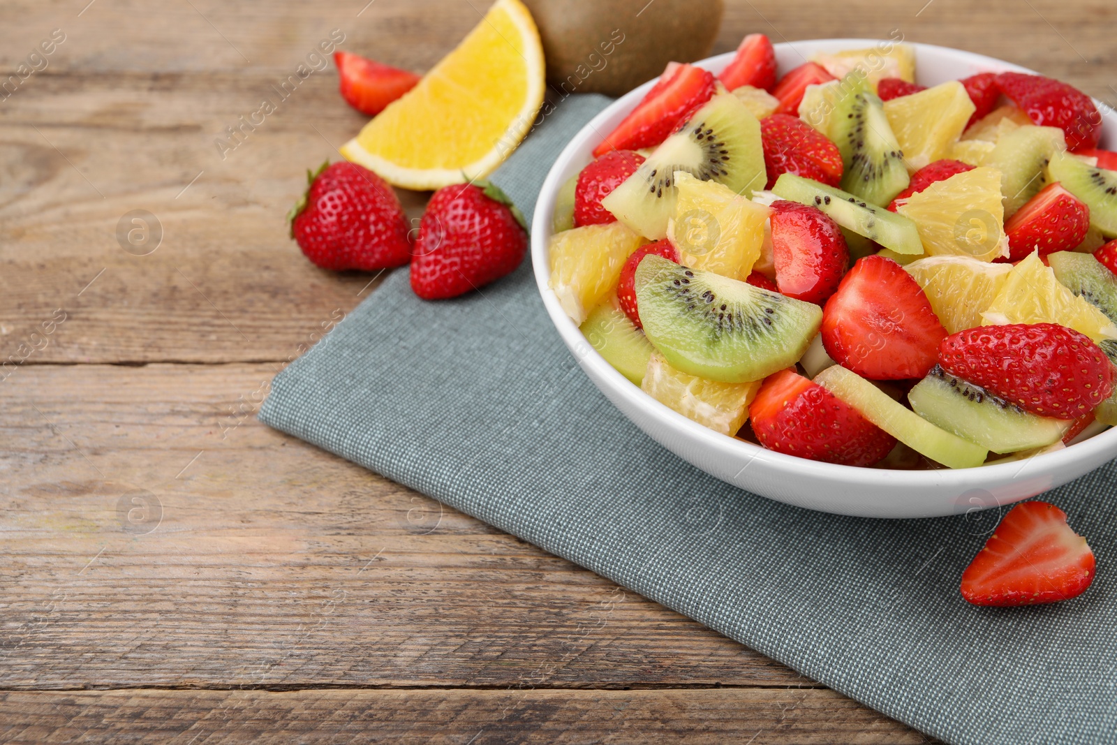 Photo of Delicious fresh fruit salad in bowl on wooden table. Space for text