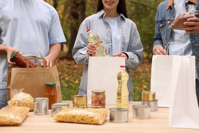 Photo of Group of volunteers packing food products at table in park, closeup