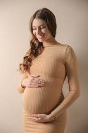 Happy pregnant woman touching her belly on beige background