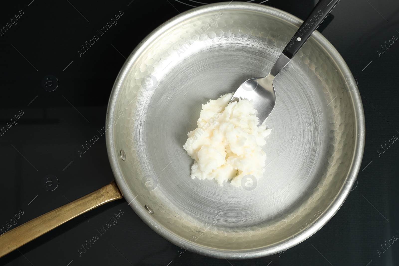 Photo of Frying pan with coconut oil and spoon on induction stove, top view. Healthy cooking