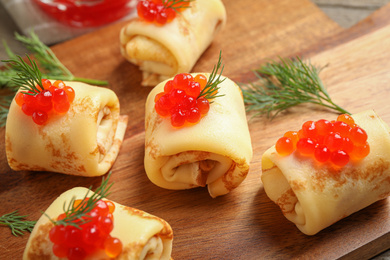 Delicious thin pancakes with red caviar on wooden board, closeup