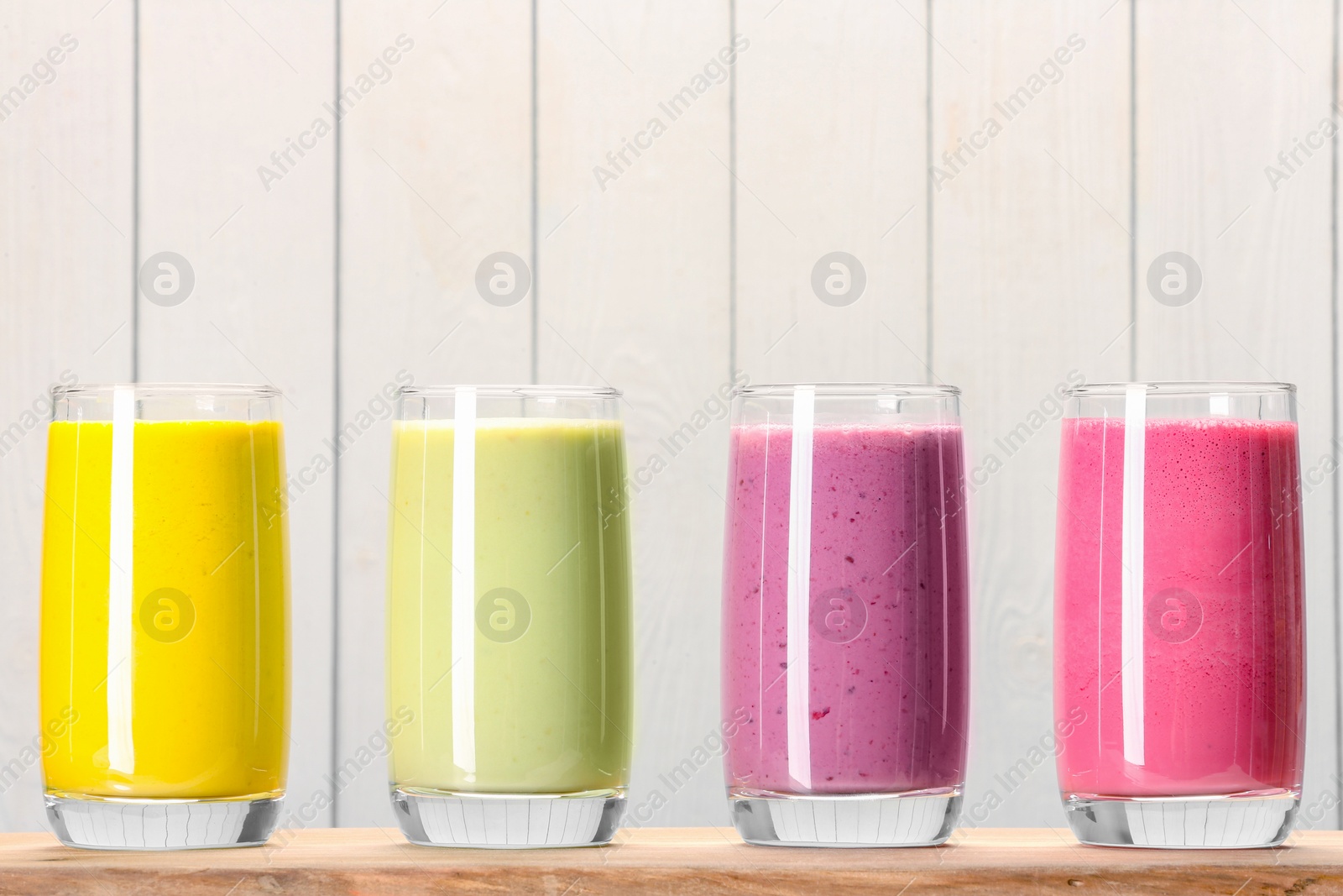 Photo of Board with many different tasty smoothies against white wooden background, space for text