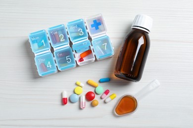 Photo of Bottle of syrup, dosing spoon and pills on white wooden table, flat lay. Cold medicine