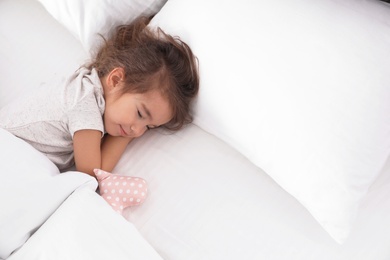 Cute little girl with toy sleeping in bed, view from above