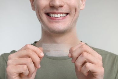 Young man with whitening strips on light grey background, closeup