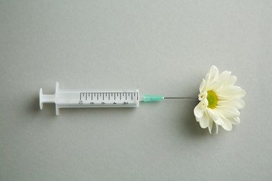 Photo of Medical syringe and beautiful chrysanthemum flower on grey background, top view