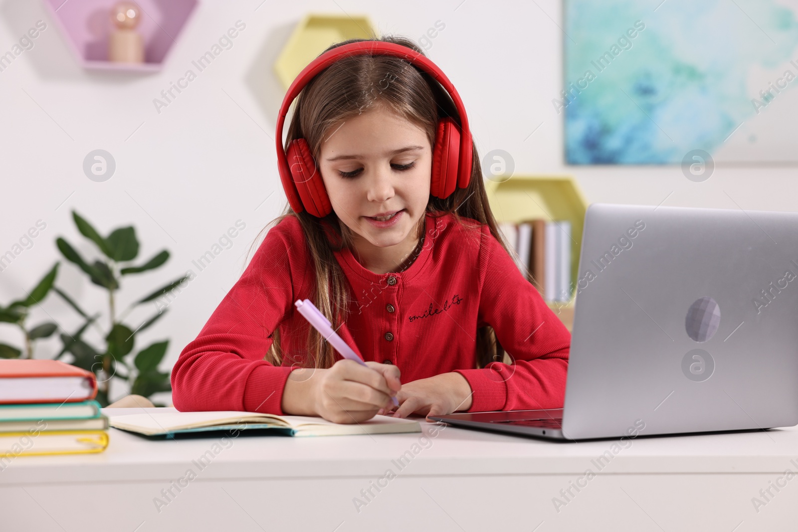 Photo of E-learning. Cute girl taking notes during online lesson at table indoors