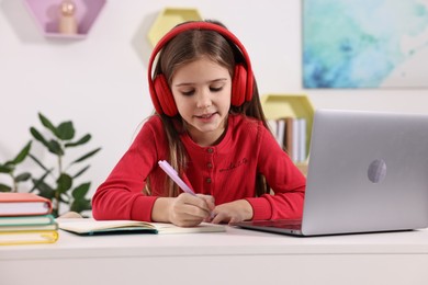 Photo of E-learning. Cute girl taking notes during online lesson at table indoors