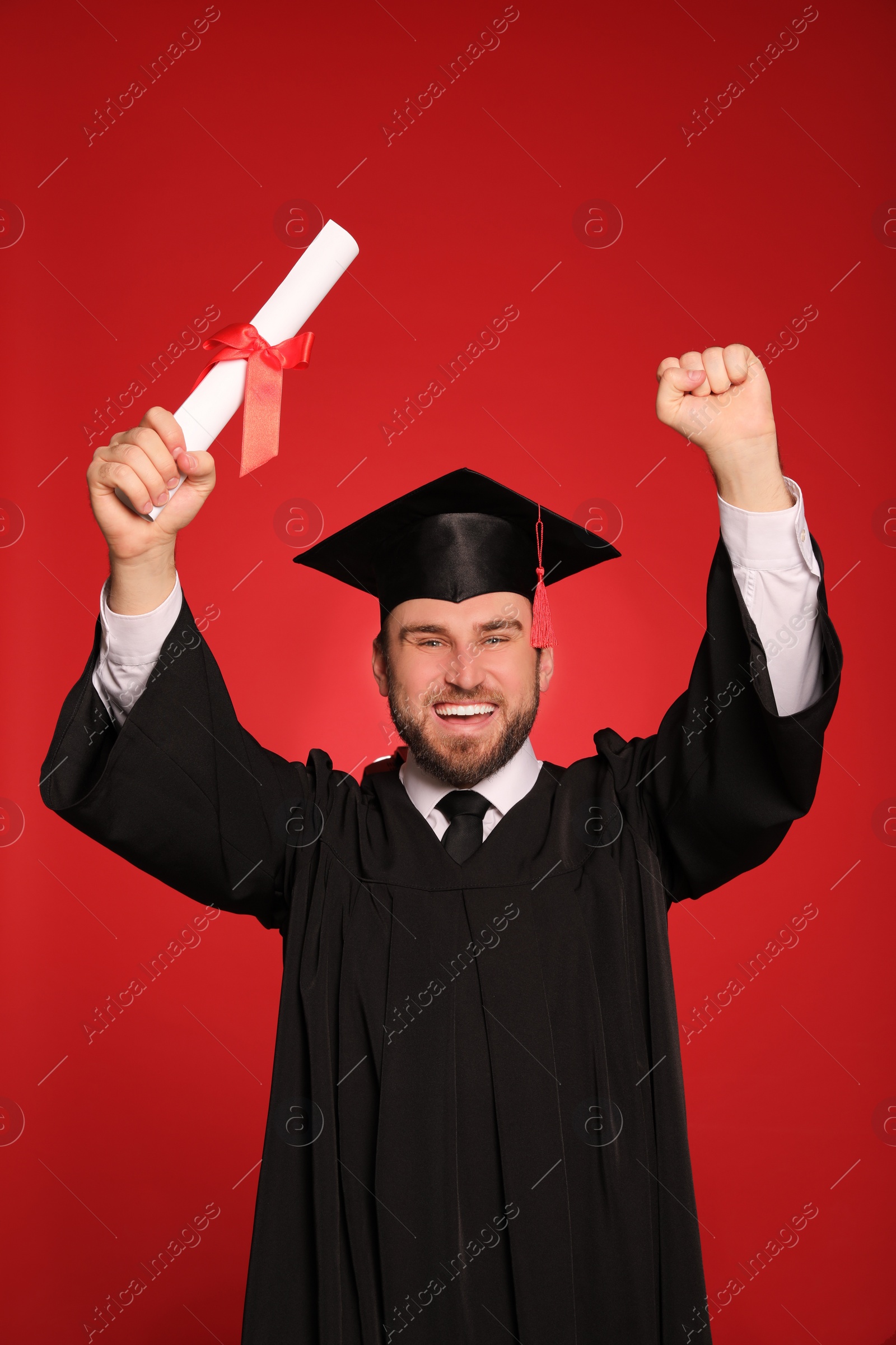 Photo of Happy student with graduation hat and diploma on red background