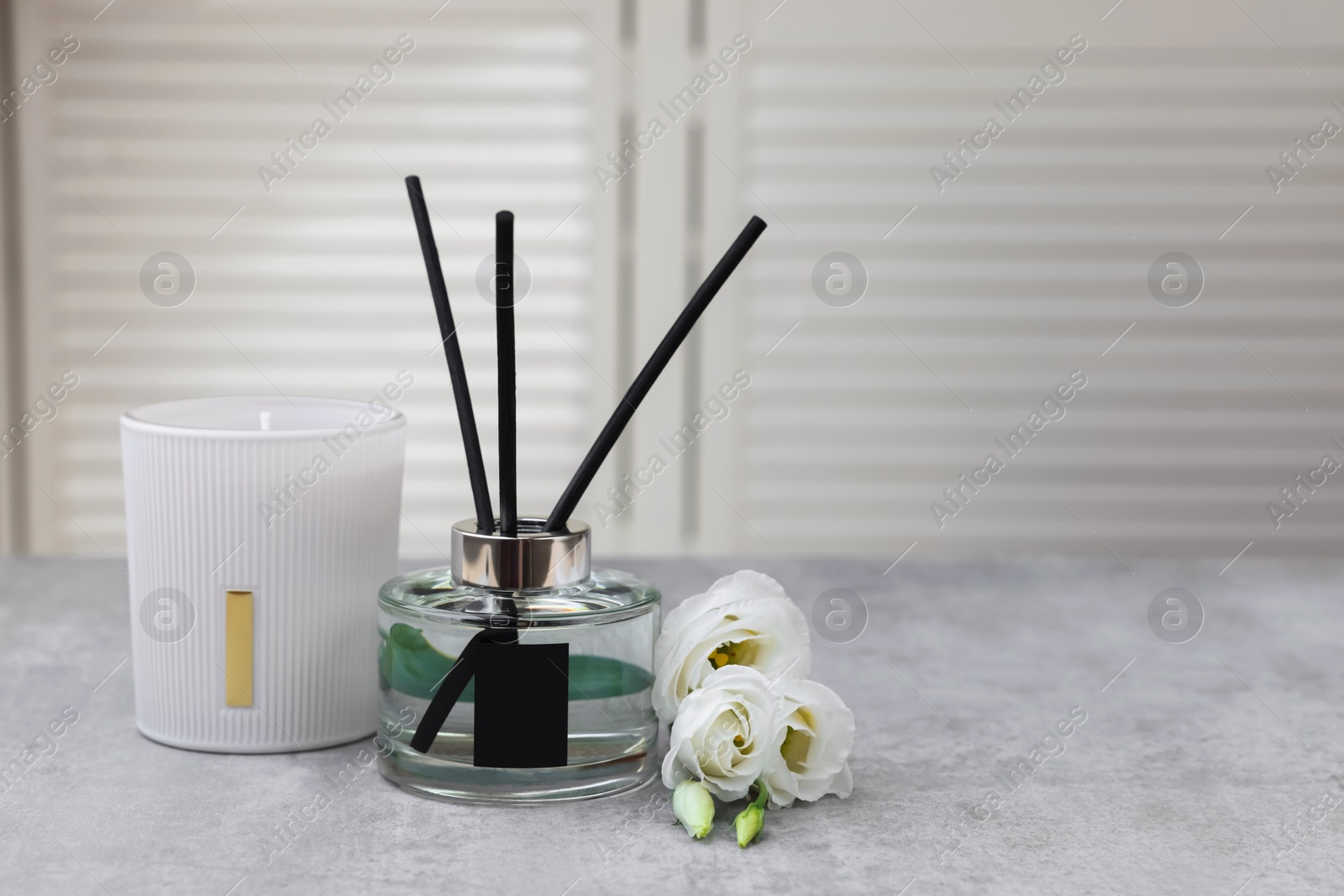 Photo of Reed diffuser, scented candle and eustoma flowers on gray marble table, space for text