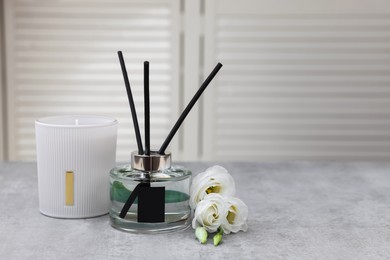 Reed diffuser, scented candle and eustoma flowers on gray marble table, space for text