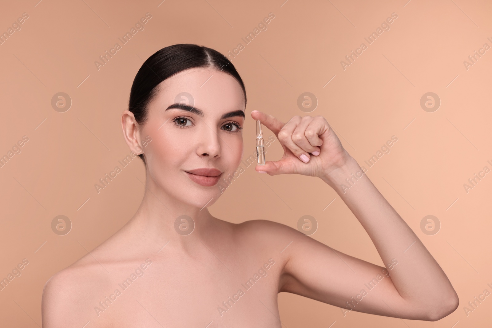 Photo of Beautiful young woman holding skincare ampoule on beige background