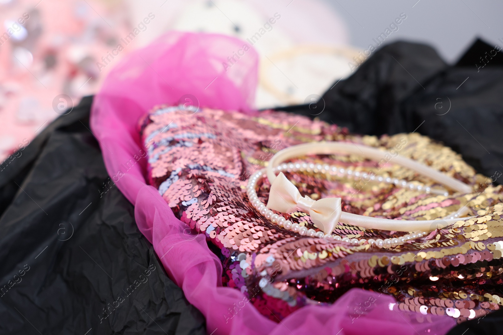 Photo of Headbands and stylish pink carnival costume with sequins in black box, closeup