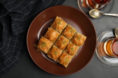 Delicious sweet baklava and hot tea on black table, flat lay