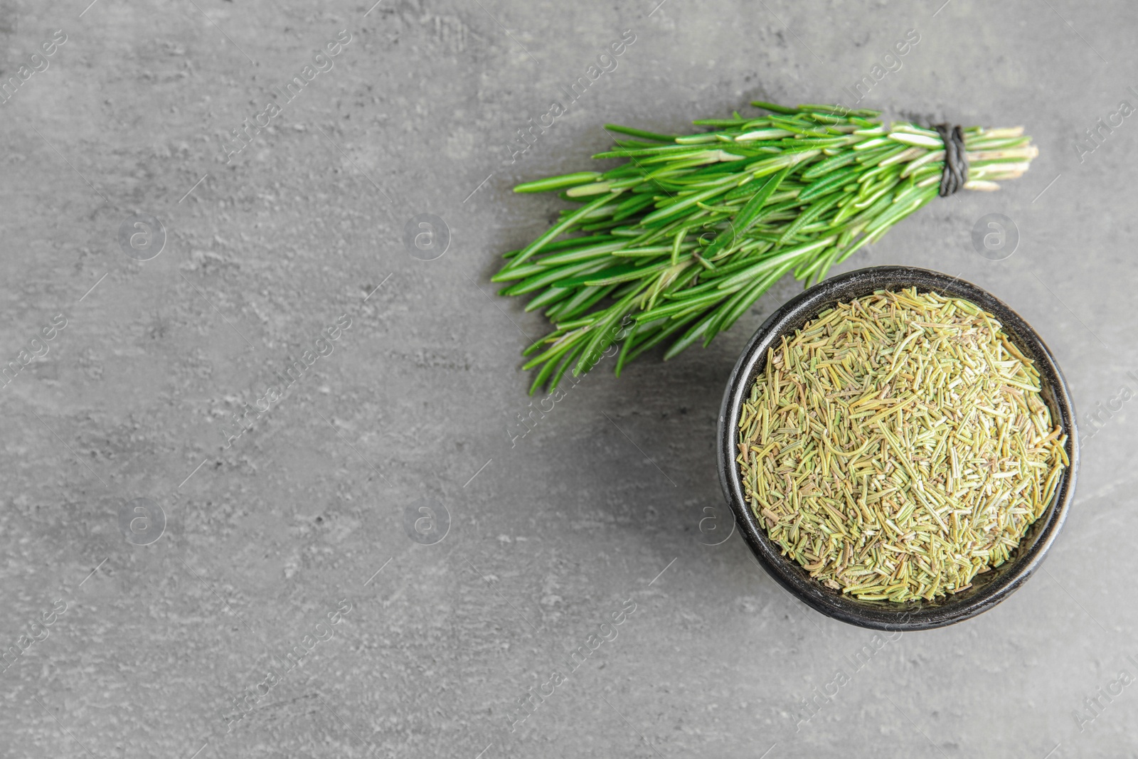 Photo of Bowl of dried rosemary and fresh bunch on grey table, flat lay. Space for text