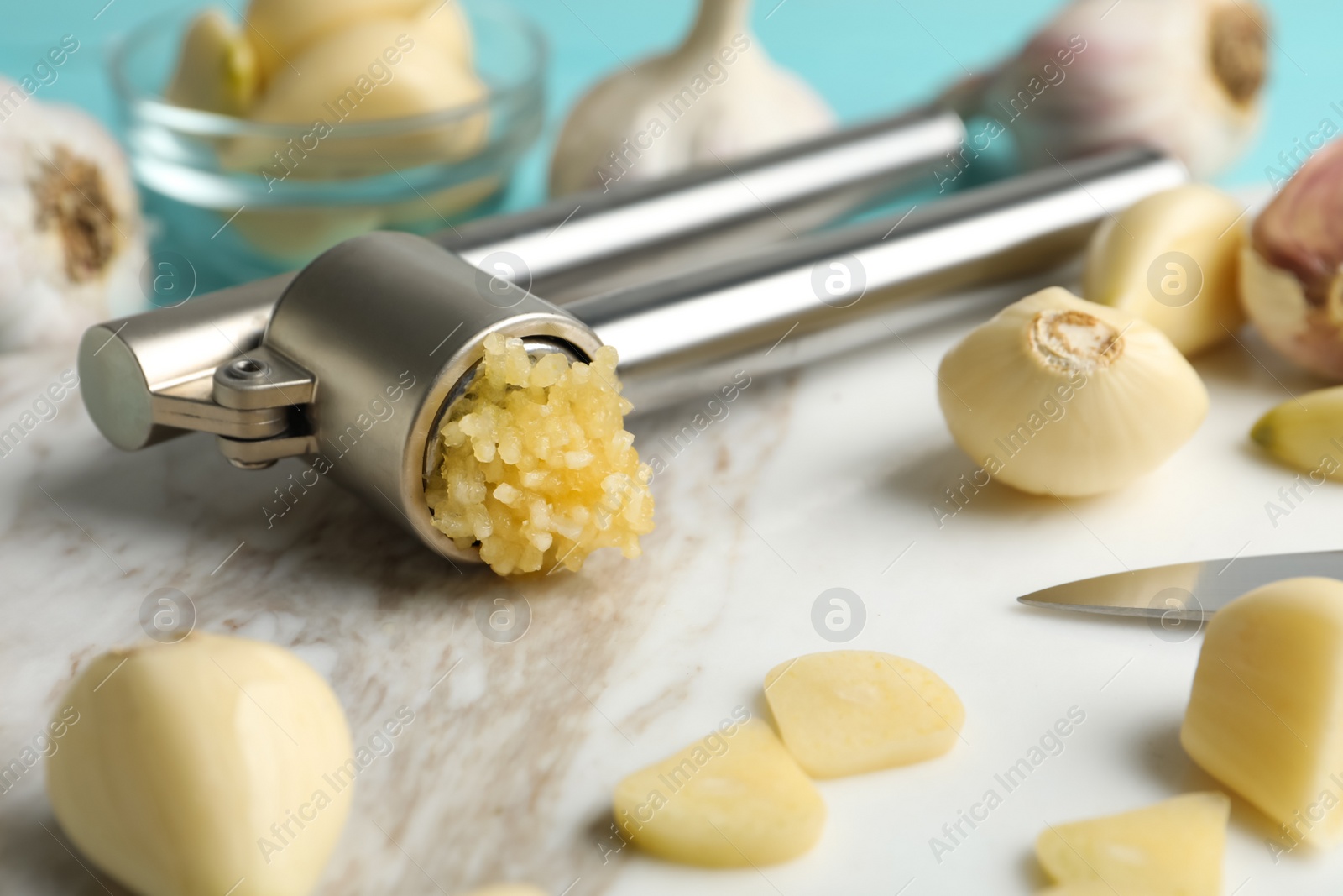 Photo of Garlic press and fresh cloves on marble board, closeup. Organic product