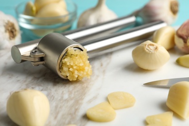 Photo of Garlic press and fresh cloves on marble board, closeup. Organic product