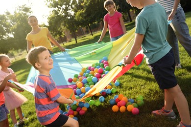 Photo of Group of children and teacher playing with rainbow playground parachute on green grass. Summer camp activity