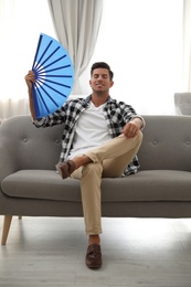 Photo of Man with hand fan sitting on sofa. Summer season