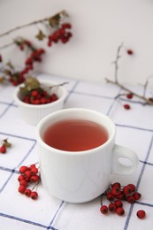 Cup with hawthorn tea and berries on table
