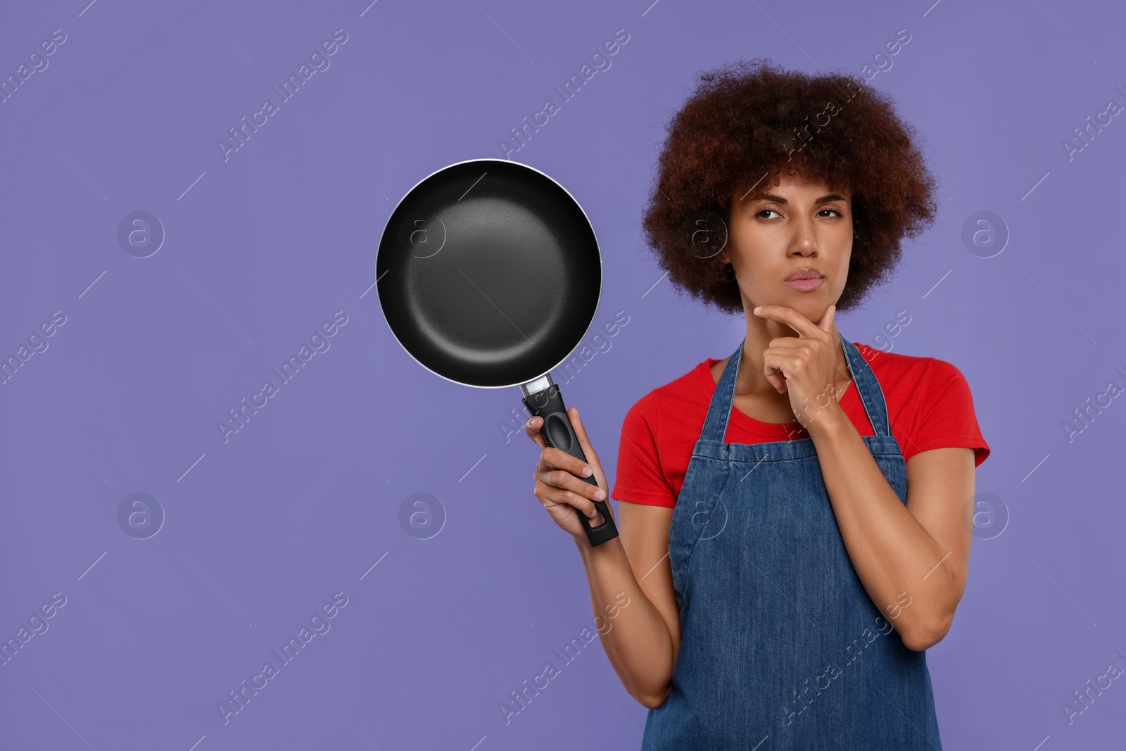 Photo of Thoughtful young woman in apron holding frying pan on purple background. Space for text