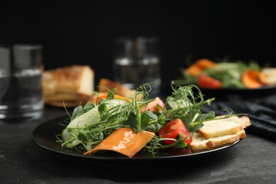 Photo of Delicious vegetable salad with microgreens served on black table