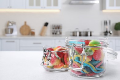 Glass jars with tasty gummy candies on white table in kitchen. Space for text
