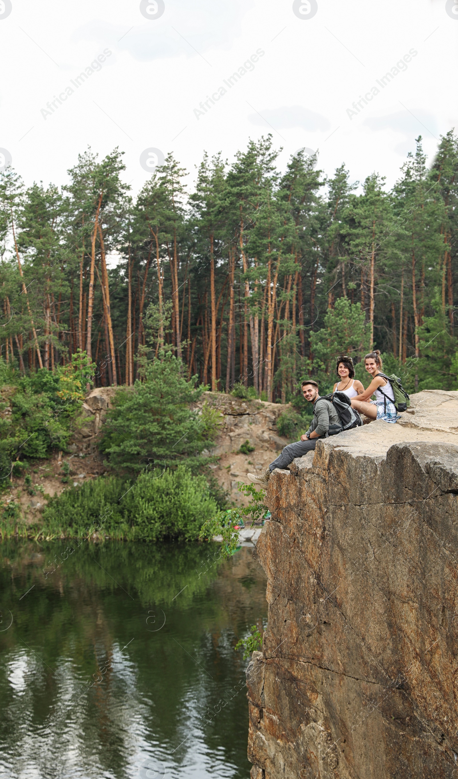 Photo of Young friends on rocky mountain near lake. Camping season