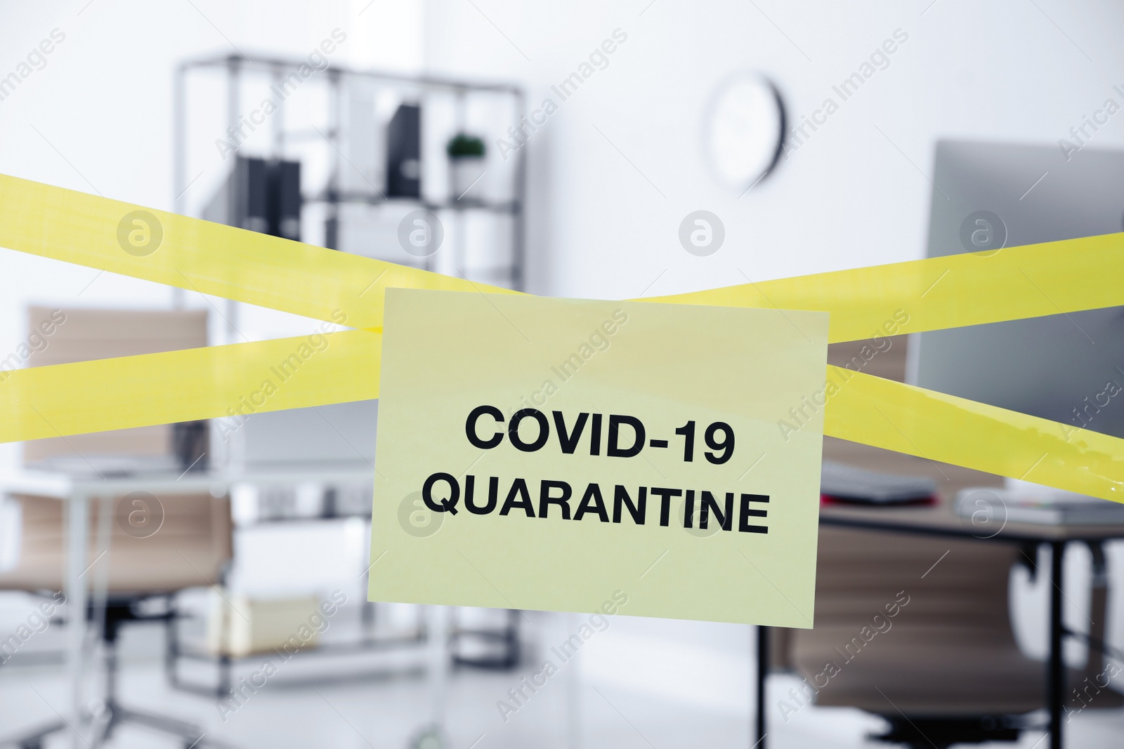 Photo of Sheet of paper with words COVID-19 Quarantine on crossed yellow tape in office