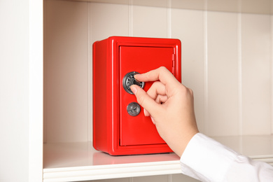 Photo of Woman opening red steel safe with mechanical combination lock, closeup