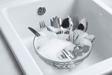 Photo of Washing silver spoons, forks and knives in kitchen sink with foam