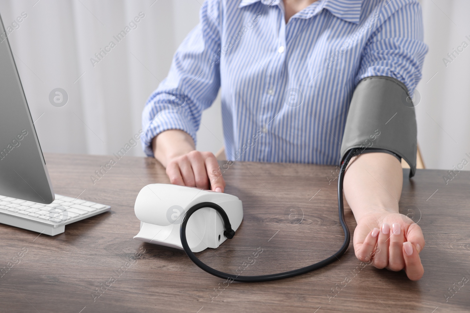 Photo of Woman measuring blood pressure at wooden table, closeup