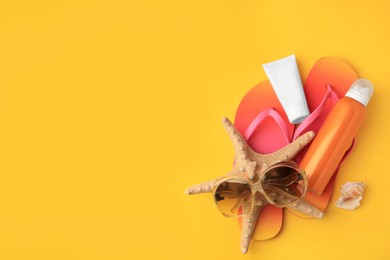 Photo of Sunscreen, sunglasses, starfish and flip flops on orange background, flat lay with space for text. Sun protection