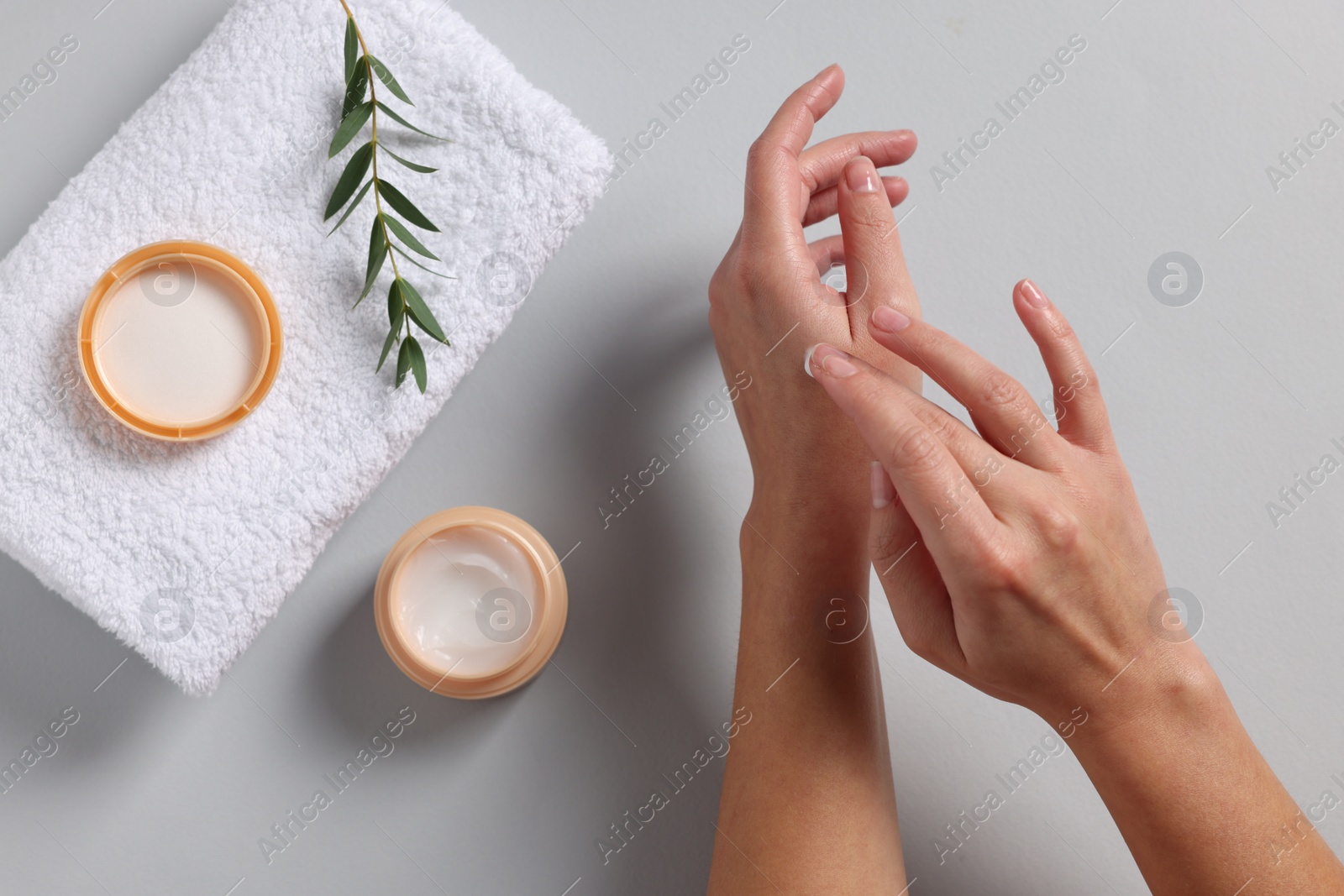 Photo of Woman with jar of hand cream, towel and green twig on light grey background, top view