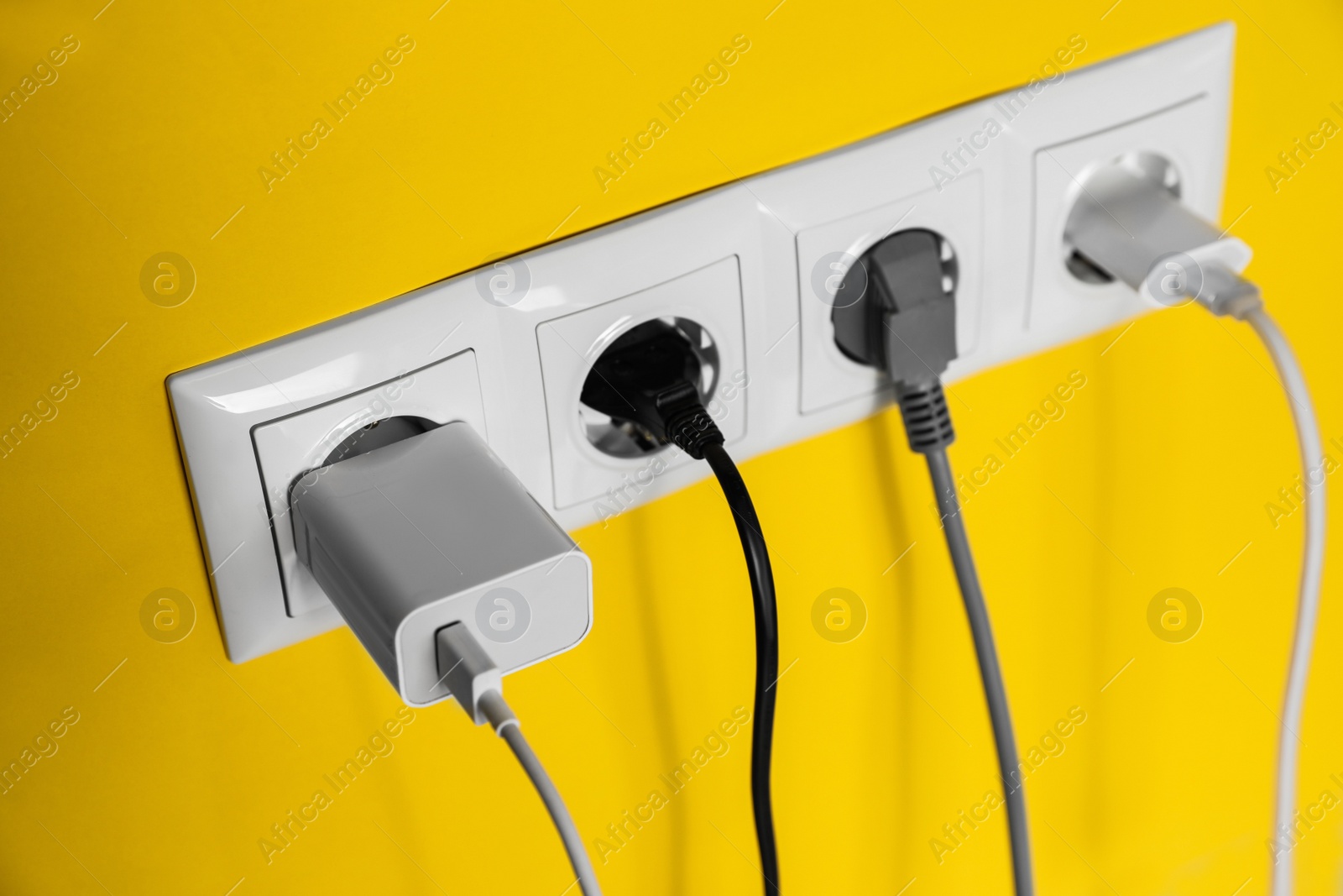 Photo of Power sockets with inserted plugs on yellow wall, closeup. Electrical supply