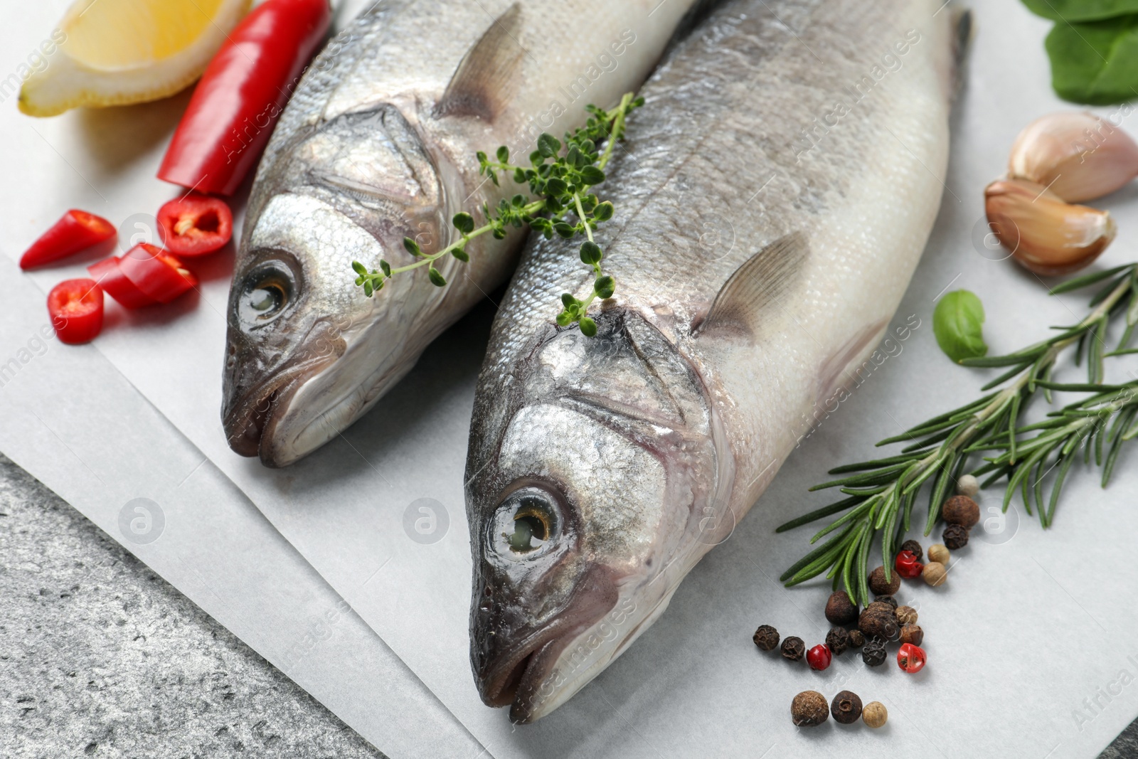 Photo of Sea bass fish and ingredients on grey table, closeup