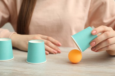 Photo of Shell game. Woman showing ball under cup at wooden table, closeup