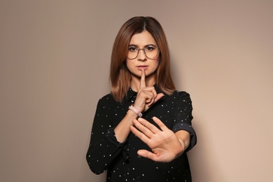 Photo of Woman showing HUSH gesture in sign language on color background