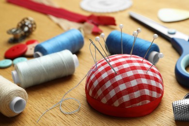 Photo of Pincushion, spools of threads and sewing tools on wooden table, closeup