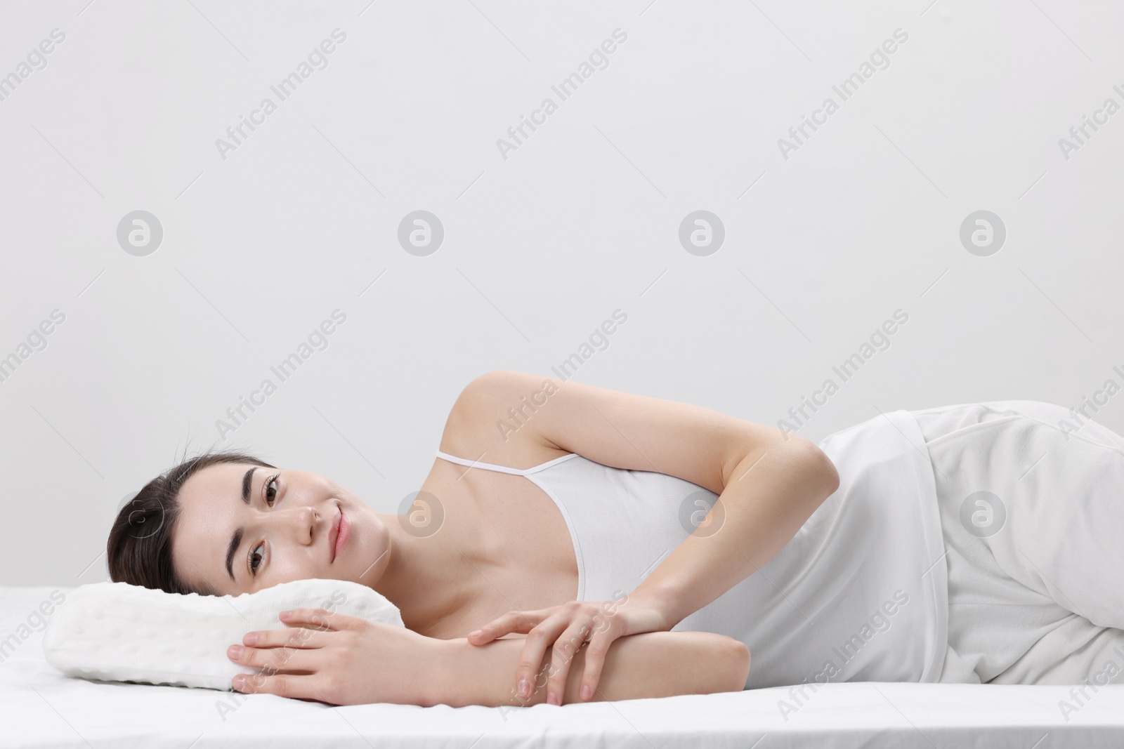 Photo of Woman lying on orthopedic pillow against light grey background, space for text