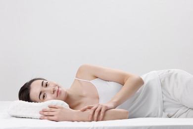 Woman lying on orthopedic pillow against light grey background, space for text