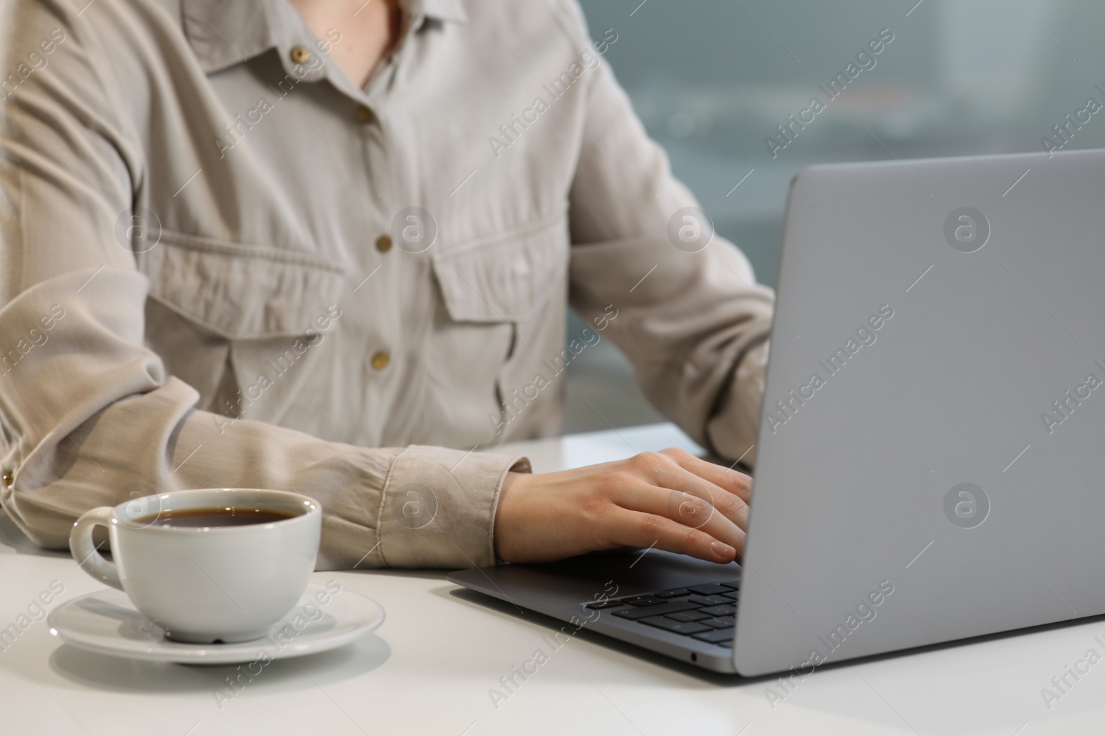 Photo of Woman working with laptop at white desk indoors, closeup