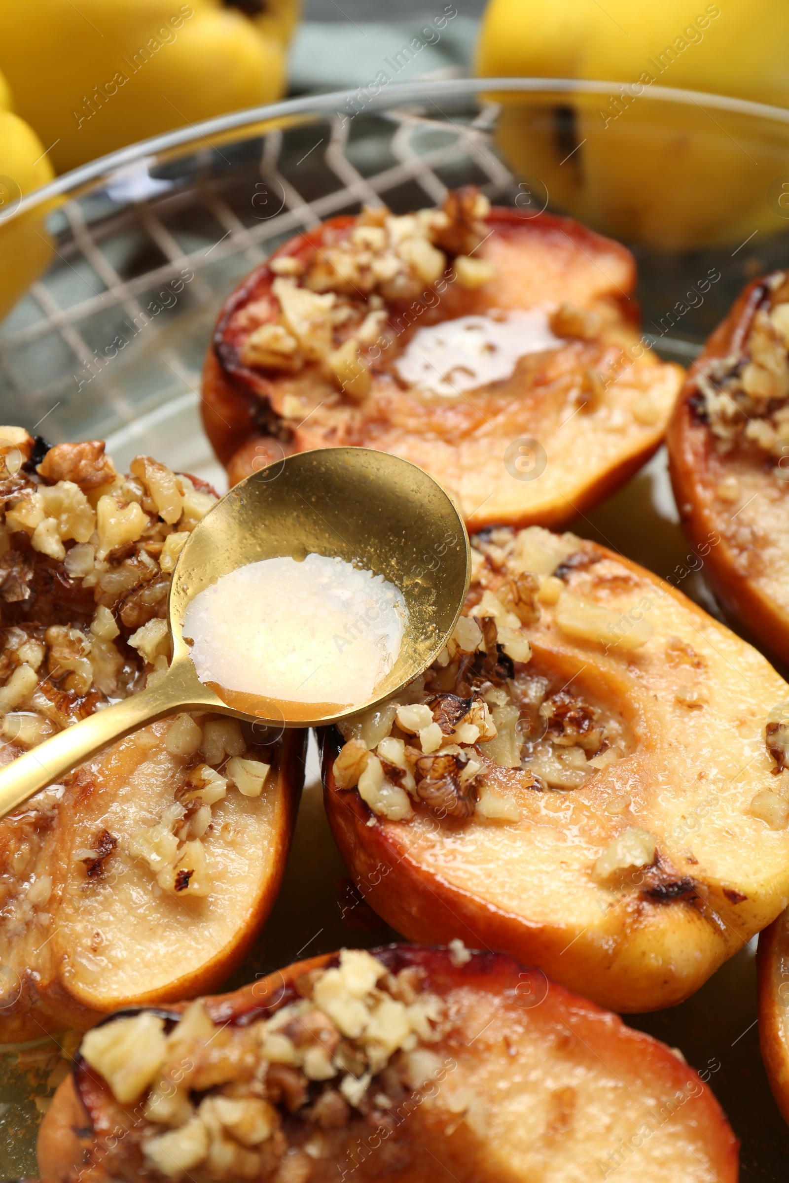 Photo of Pouring tasty honey onto baked quinces in bowl on table, closeup