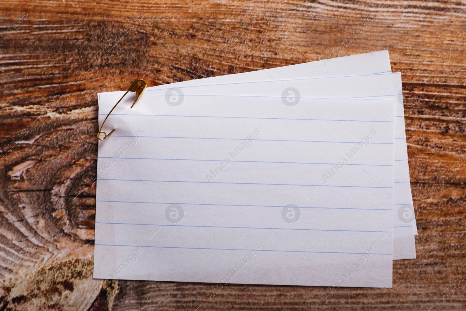 Photo of Paper sheets attached with safety pin on wooden table, top view. Space for text