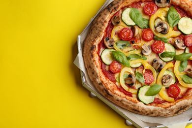 Photo of Delicious vegetable pizza in cardboard box on yellow background, top view. Space for text